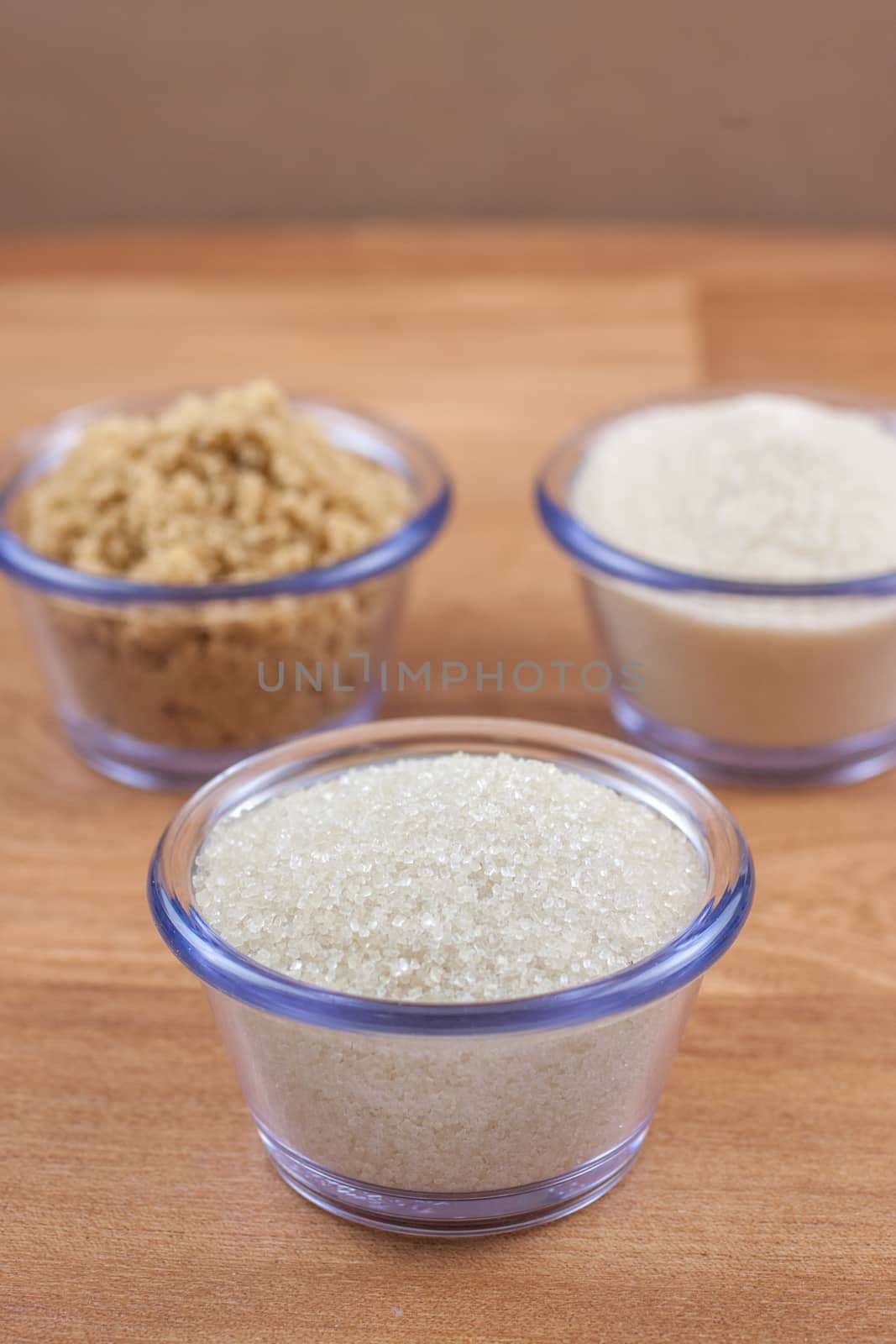 Organic crystal, brown, and fine sugar in clear bowls on a wooden surface.