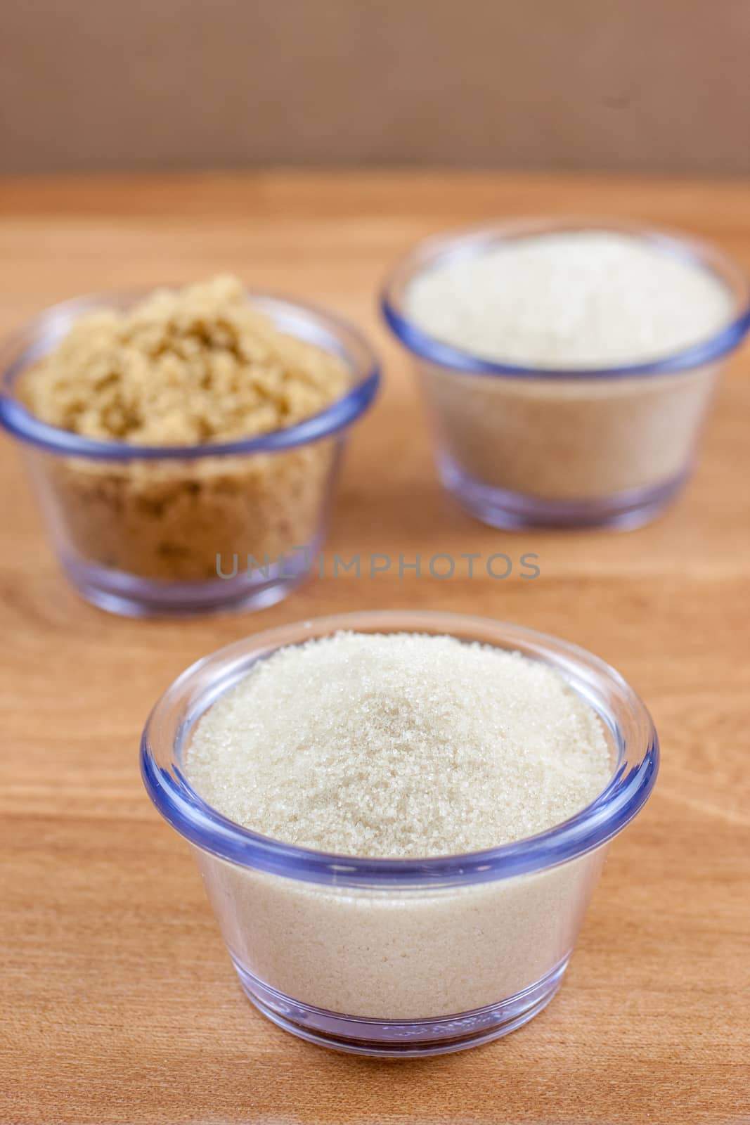 Organic crystal, brown, and fine sugar in clear bowls on a wooden surface.