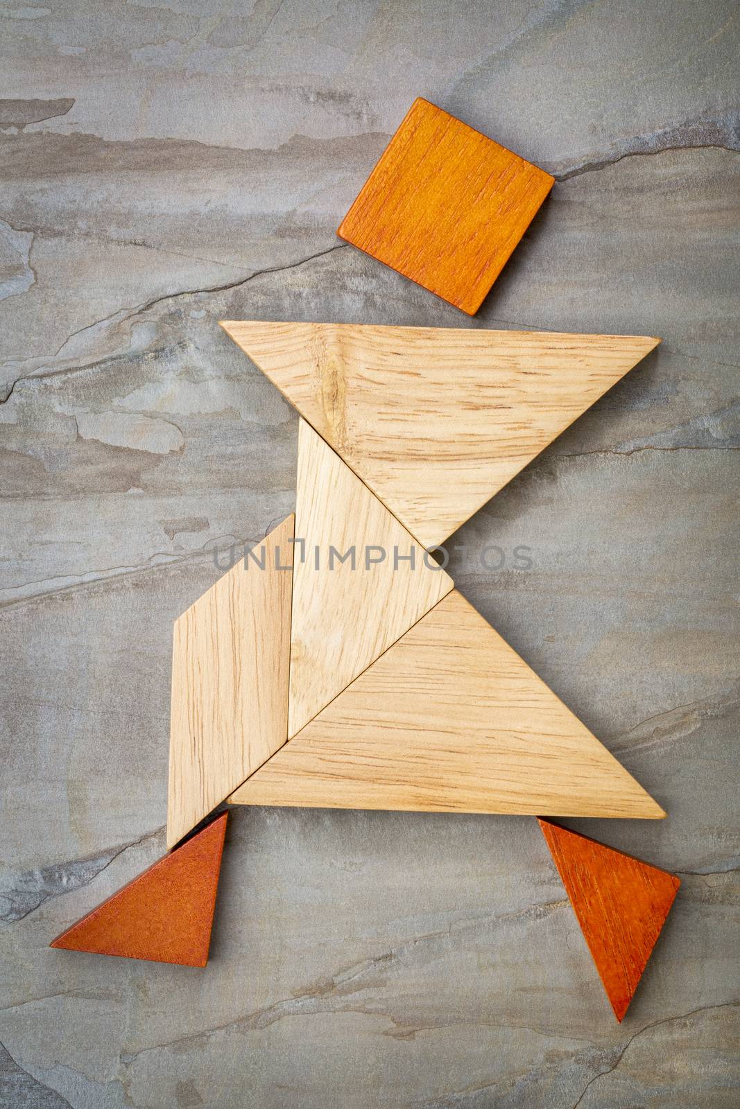 abstract of a dancing or walking figure built from seven tangram wooden pieces, a traditional Chinese puzzle game; slate rock background background, the artwork copyright by the photographer