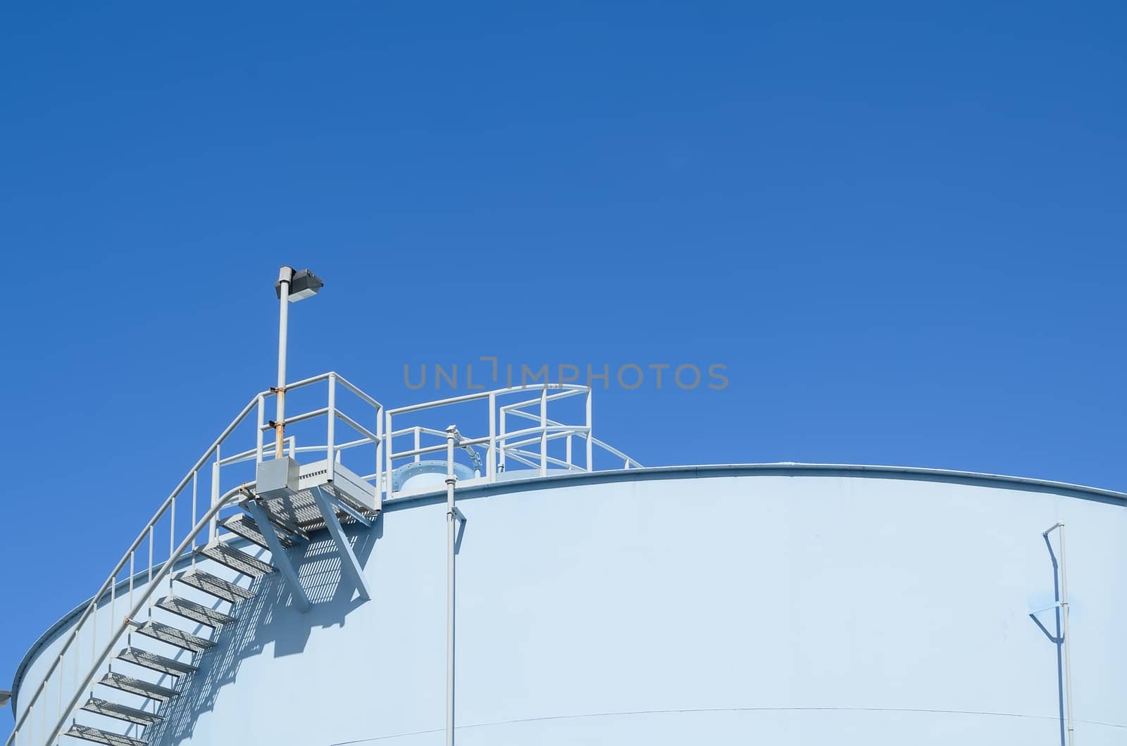 Blue industrial storage tank against cloudless blue sky