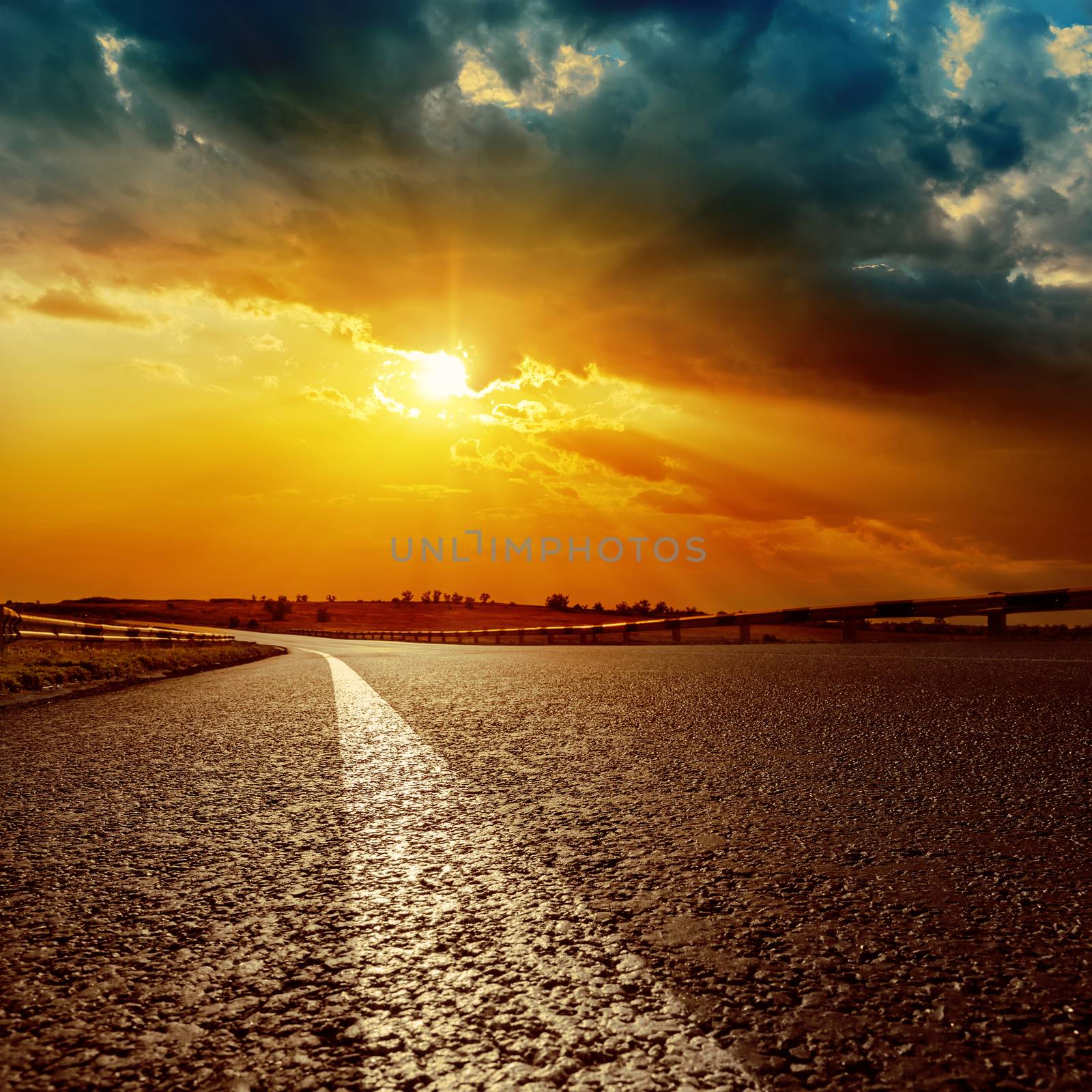 dramatic sunset and white line on asphalt road to horizon by mycola