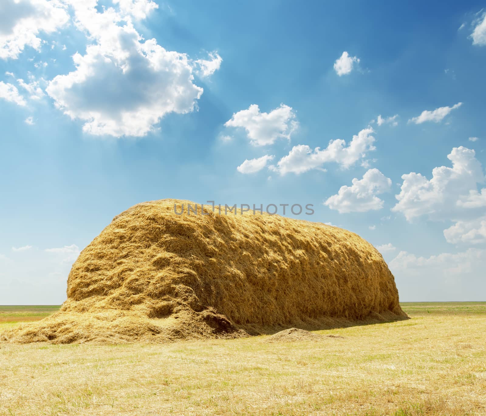stack of straw under blue sky with clouds by mycola