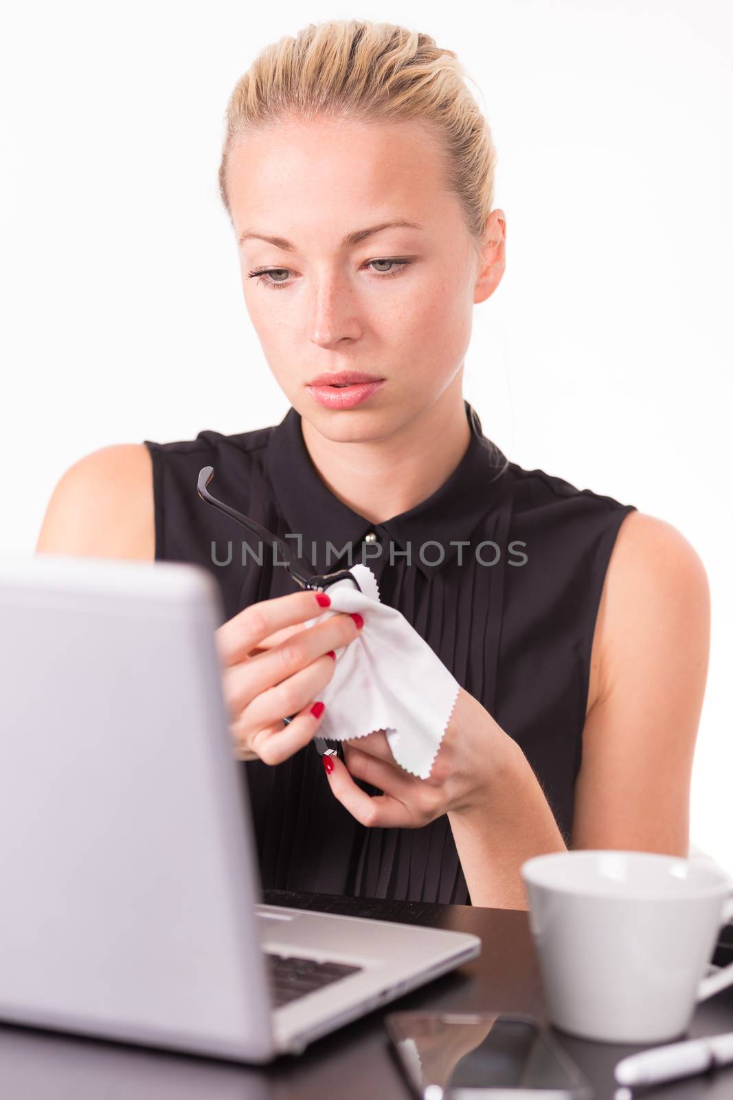 Business woman wiping her black diopter glasses while checking some information on her laptop computer in office. 