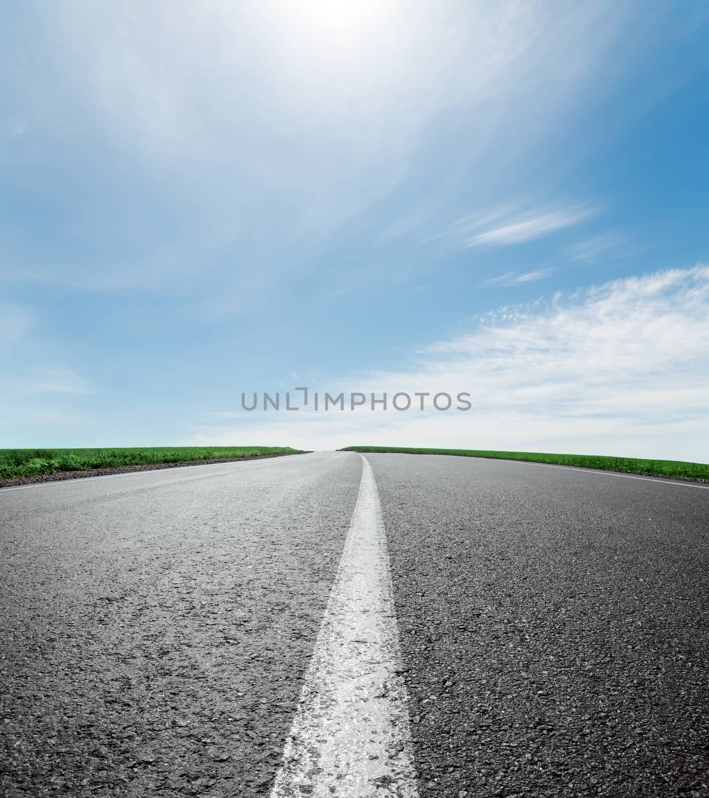 asphalt road to horizon under sky with clouds and sun by mycola