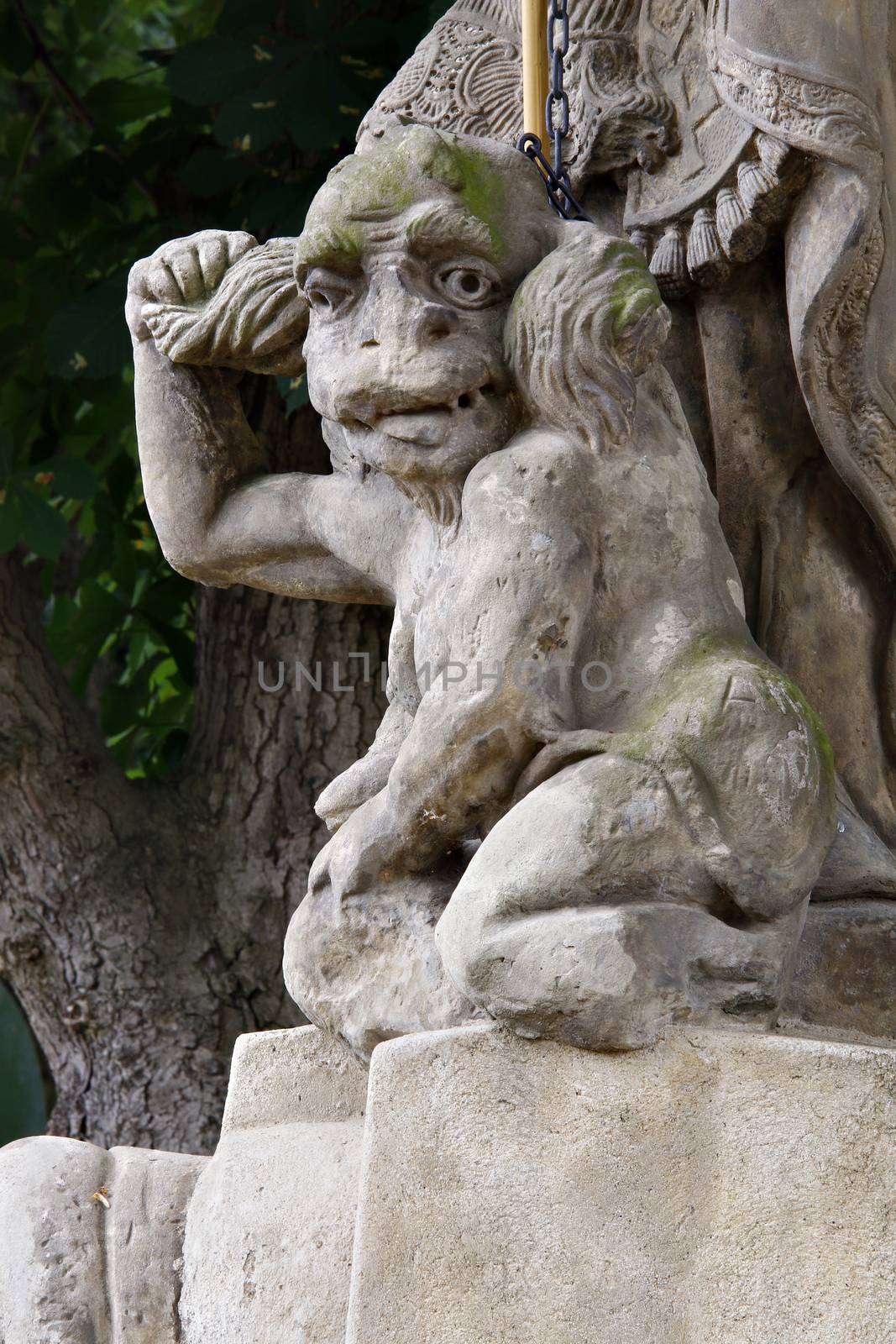 Baroque statue on the crossroad - Saint Procopius with bound devil.
Saint Procopius of Sazava (end of the 10th century Chotoun - March 25, 1053, Sazava) was originally a secular priest, later a hermit, co-founder and first abbot of the monastery Sazava. He was canonized in 1204. 
His main attribute is bound devil, which is at his feet or on which he stands.
Czech republic.