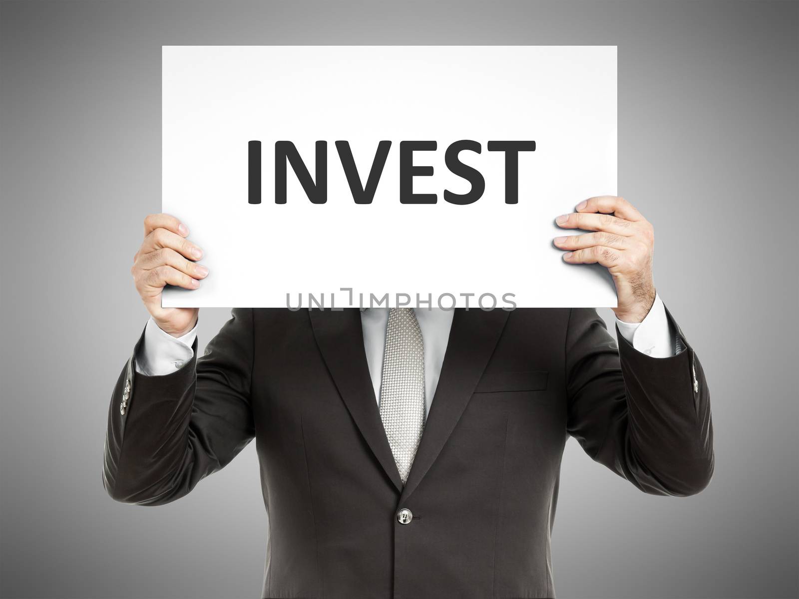 A business man holding a paper in front of his face with the word invest