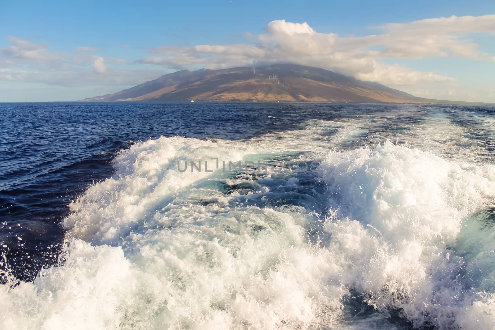 The island of Maui seenfrom the ocean over the wake of a motorboat