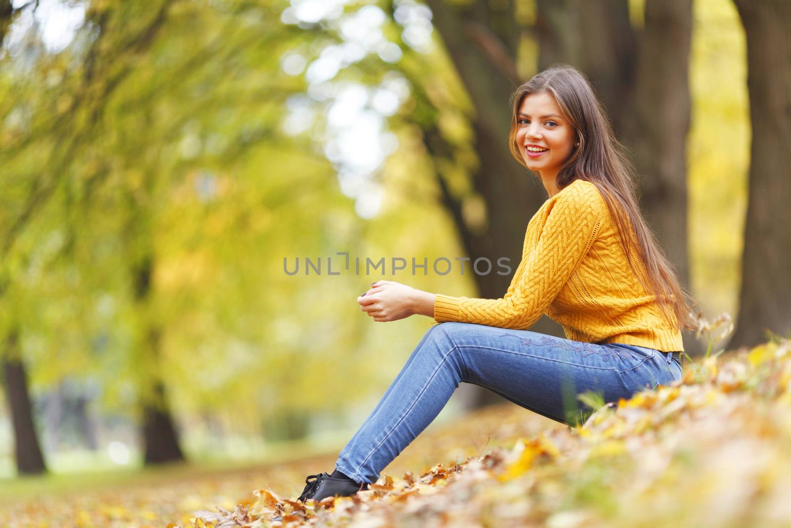 Beautiful woman sitting on autumn leaves in park