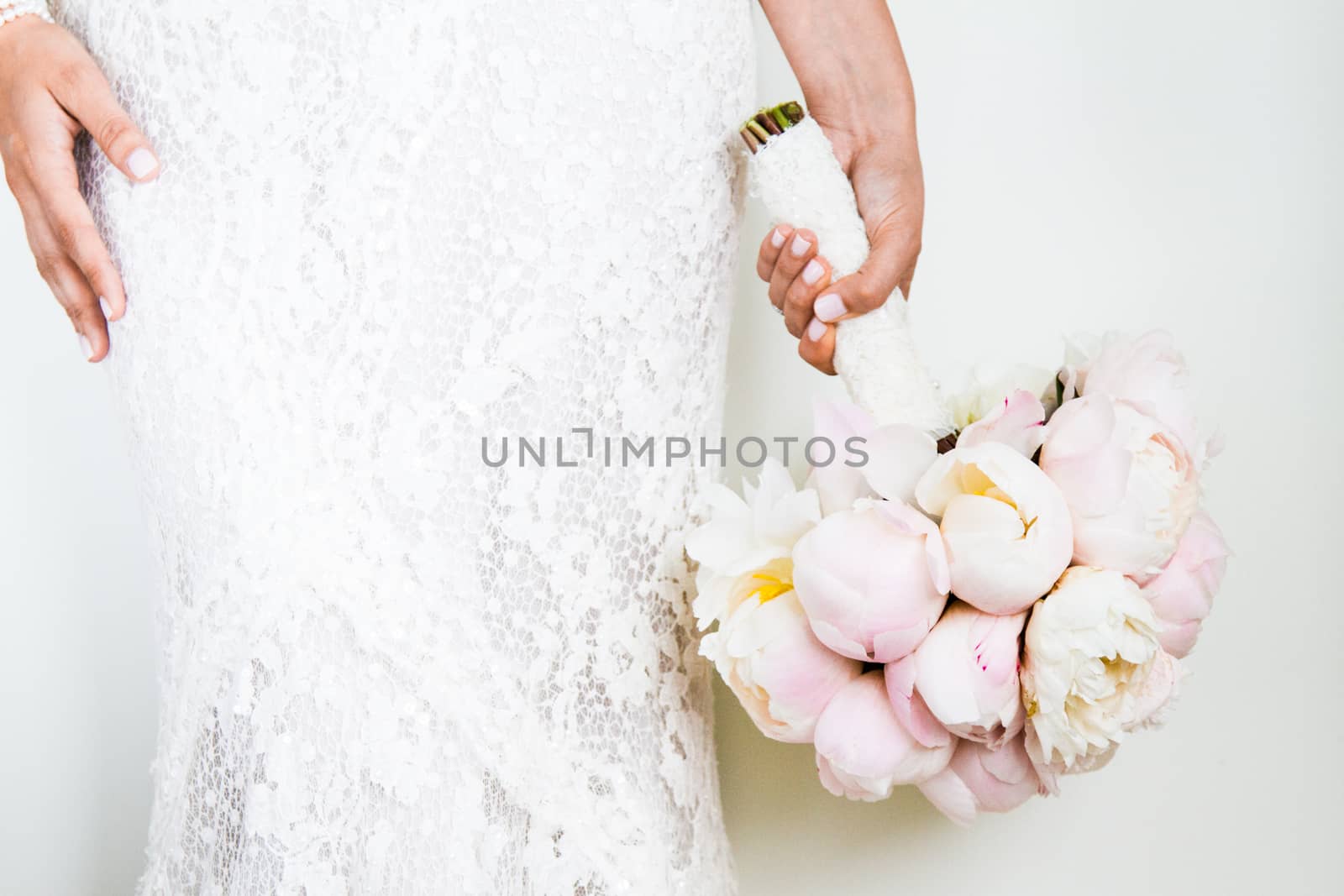 Woman Holding a nice Wedding Bouquet in front of a white Wall