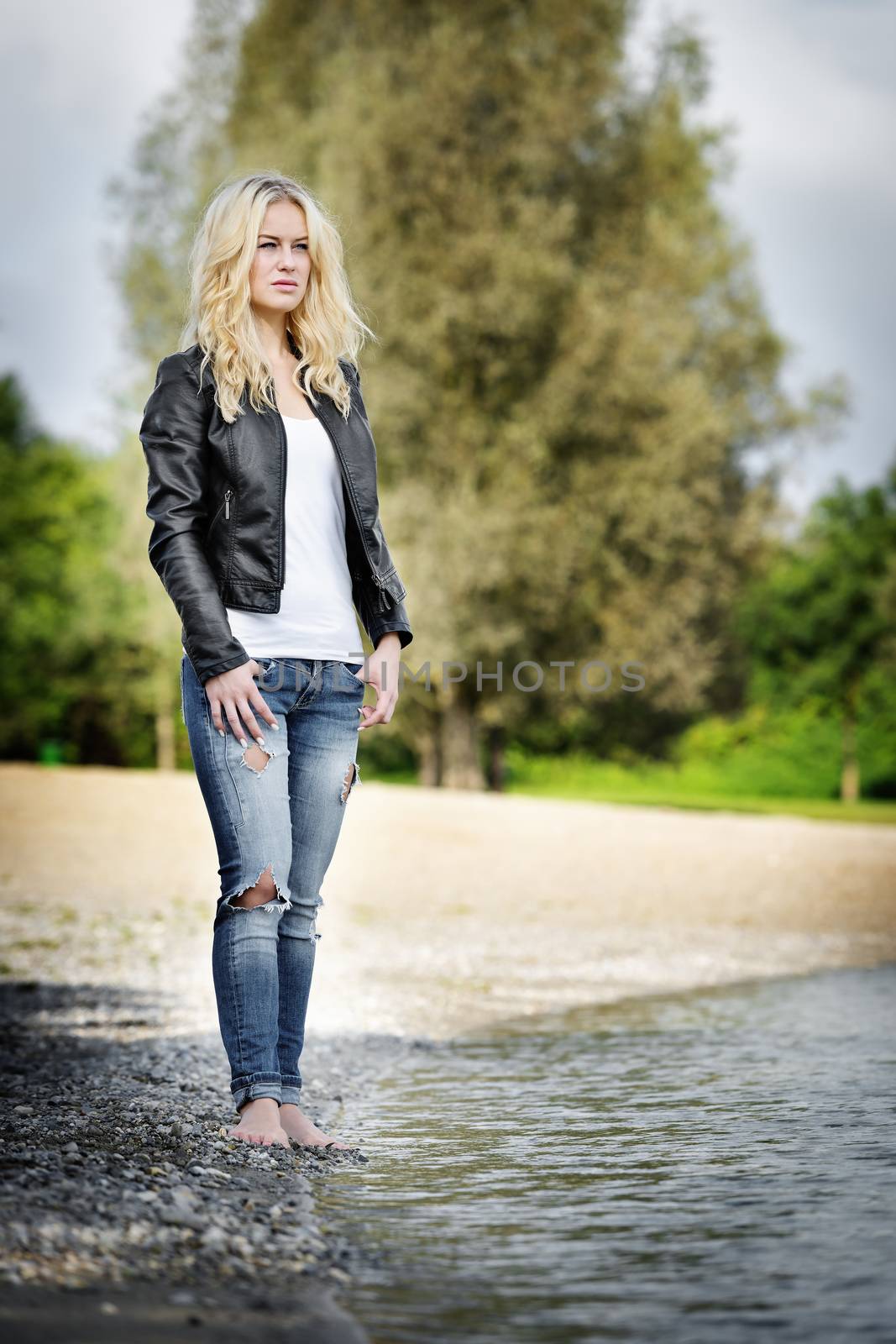 Blond young woman standing barefoot on the edge of a lake