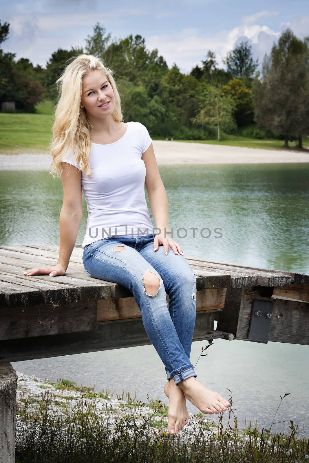 Young blond woman is sitting on a jetty at a lake in summer