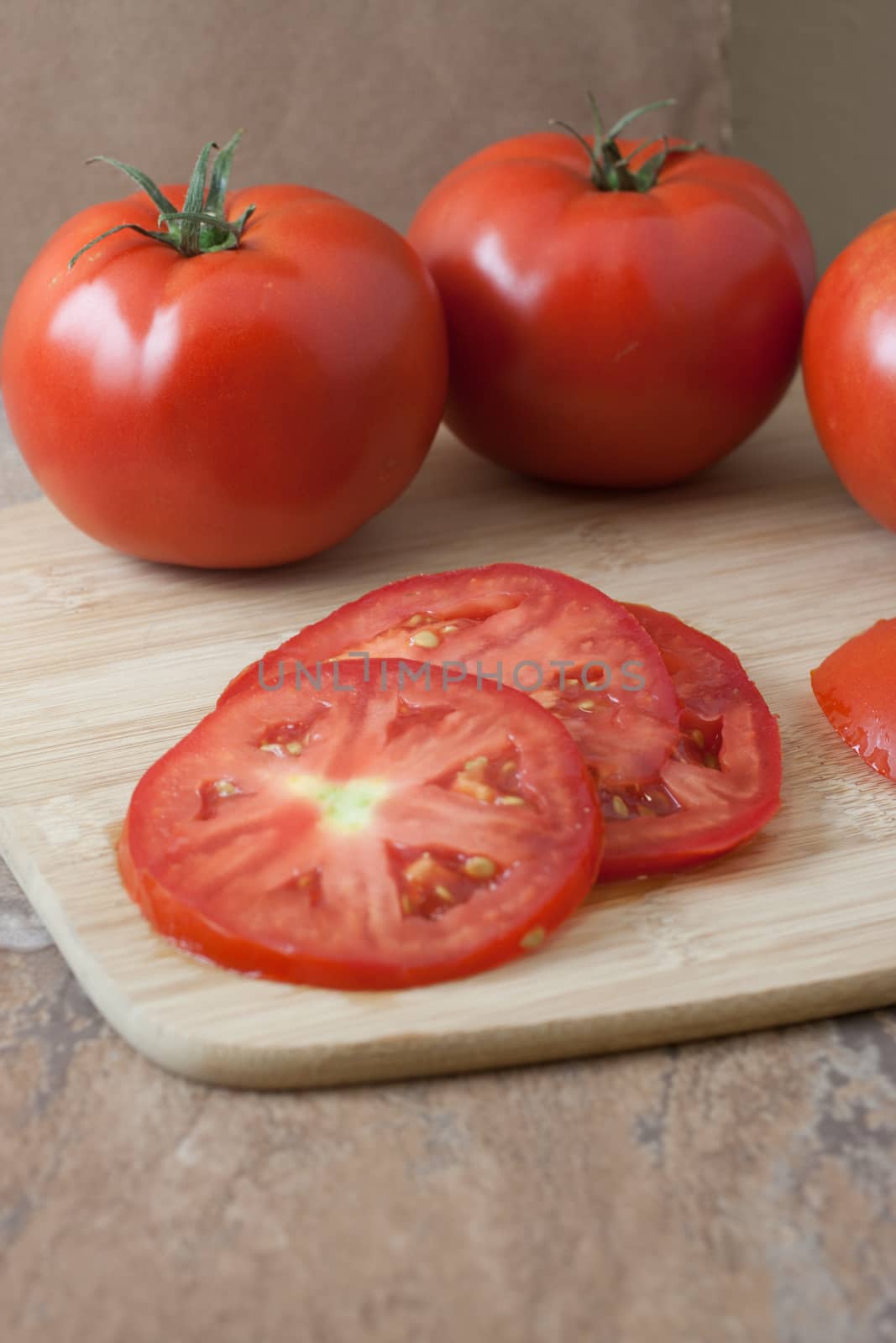 Fresh sliced tomatoes on a bamboo cutting board on a tile counter top.