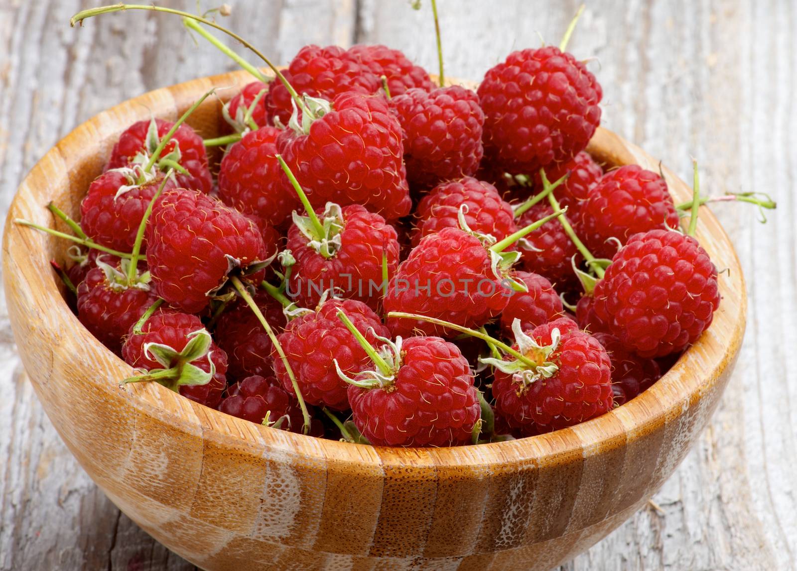 Perfect Ripe Raspberries with Stems in Wooden Bowl closeup on Rustic Wooden background