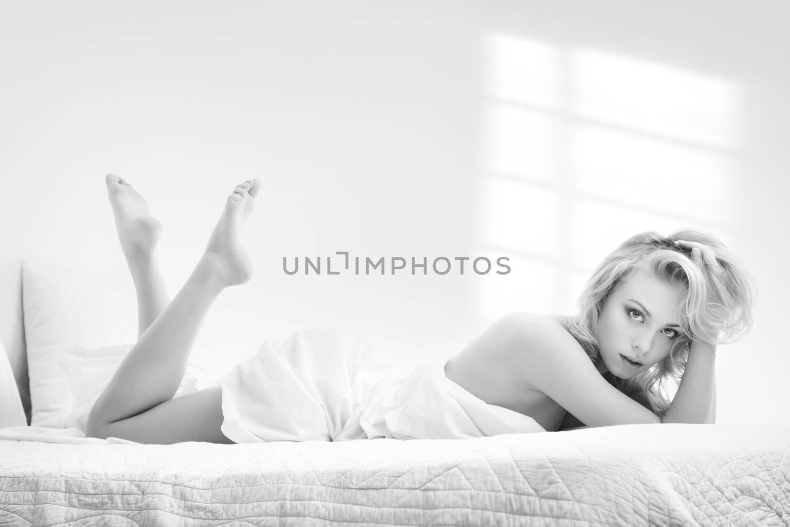 Black and white photo of the young blond lady in a bedroom with window shadows on the wall