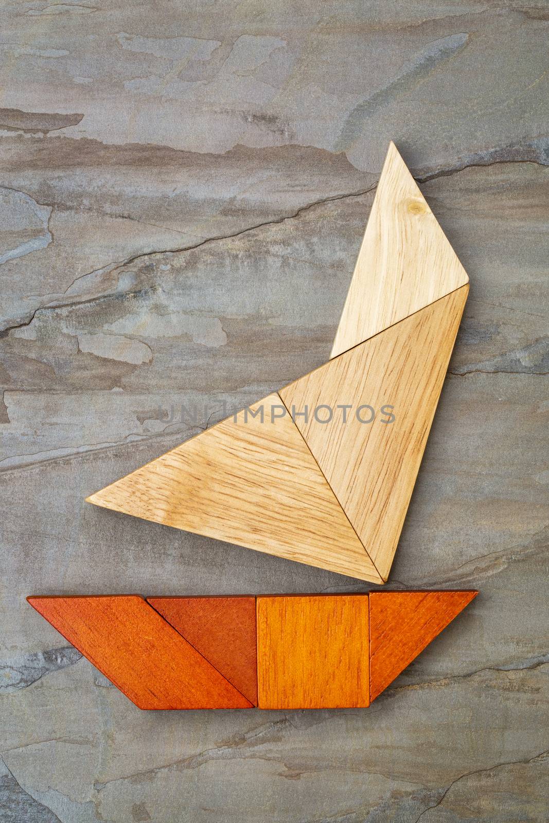 abstract picture of a sailing yacht built from seven tangram wooden pieces over a slate rock background, artwork created by the photographer