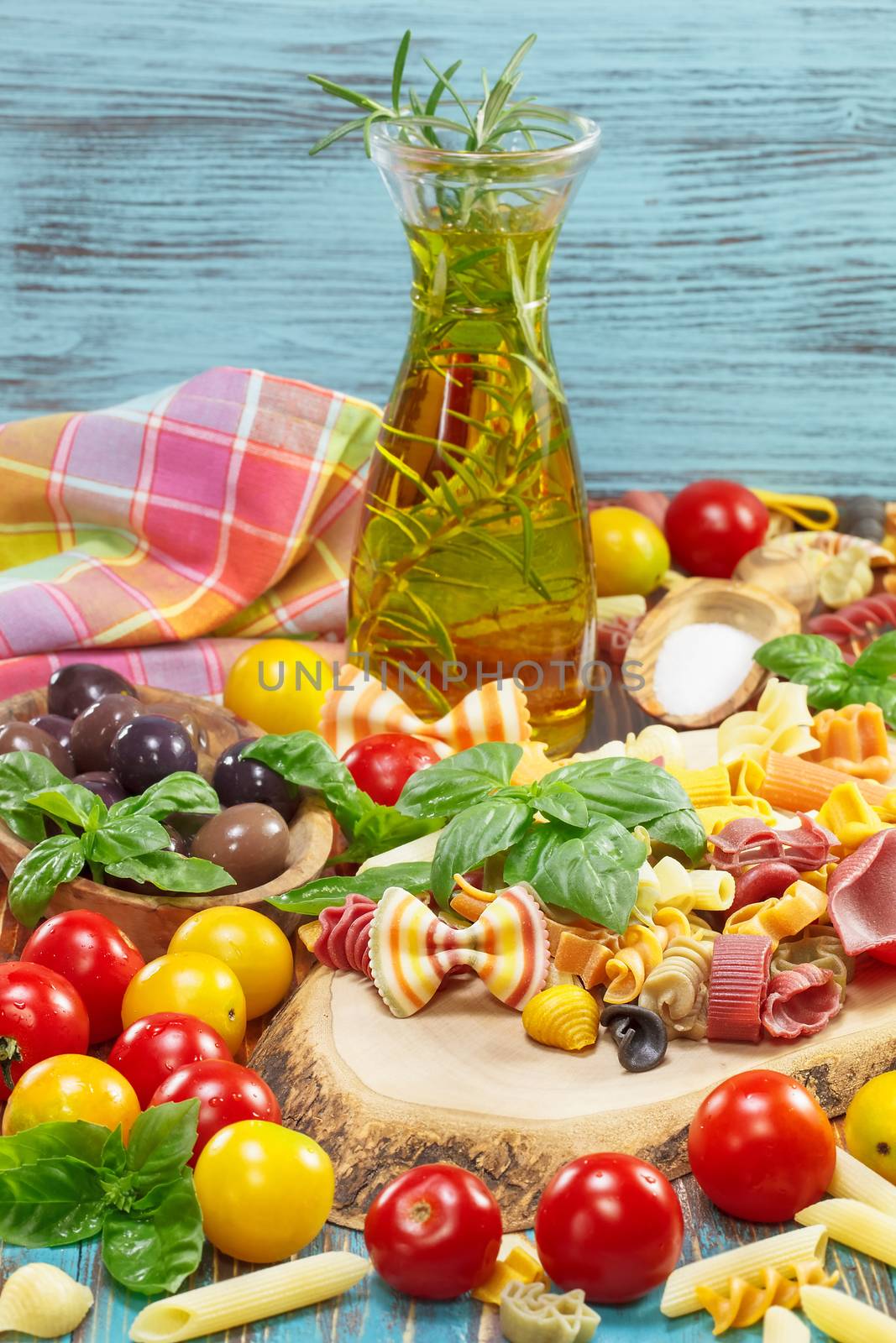 Variety of uncooked pasta and vegetables. Fresh ingredients for making pasta dish with a herbs, olive oil, olives, tomatoes and uncooked pasta different colors