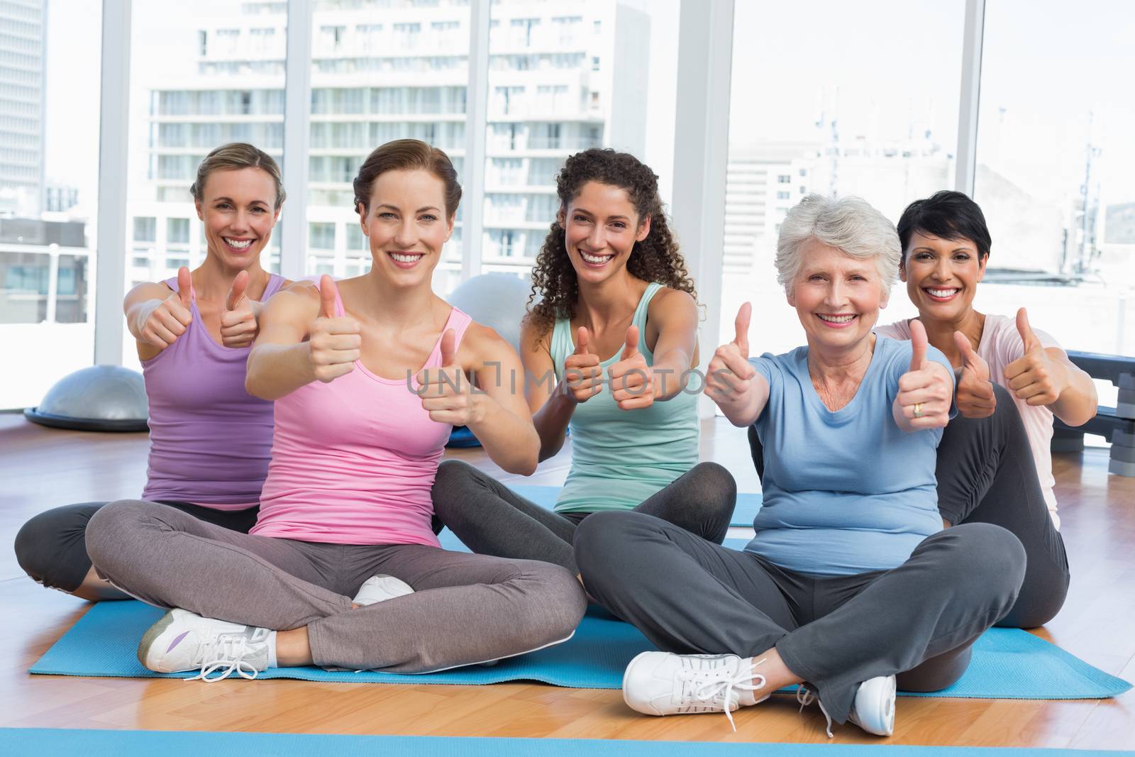 Full length portrait of happy women gesturing thumbs up in the yoga class
