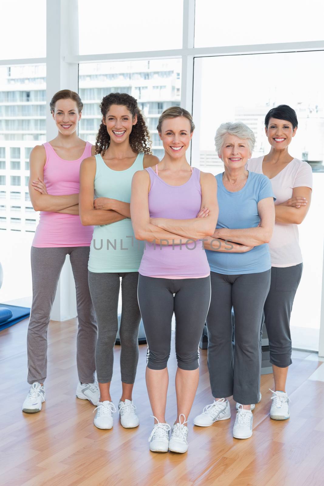 Happy women with arms crossed in yoga class by Wavebreakmedia