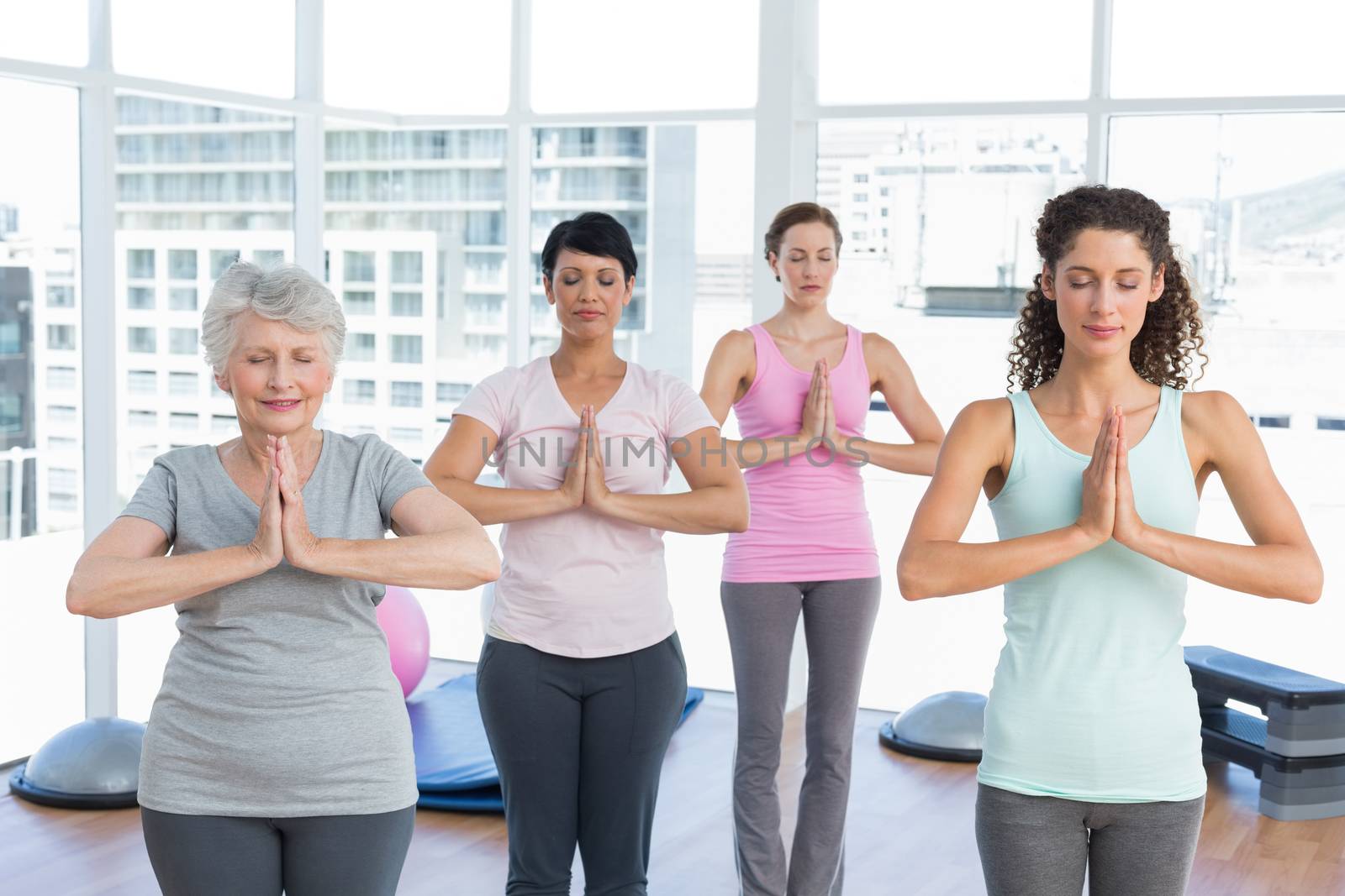 Female trainer with class standing in namaste pose at yoga class