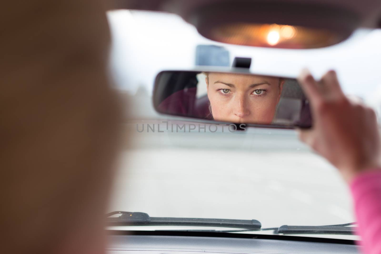Beautiful young lady looking back through the rear view mirror from the front seat of a car while reversing.