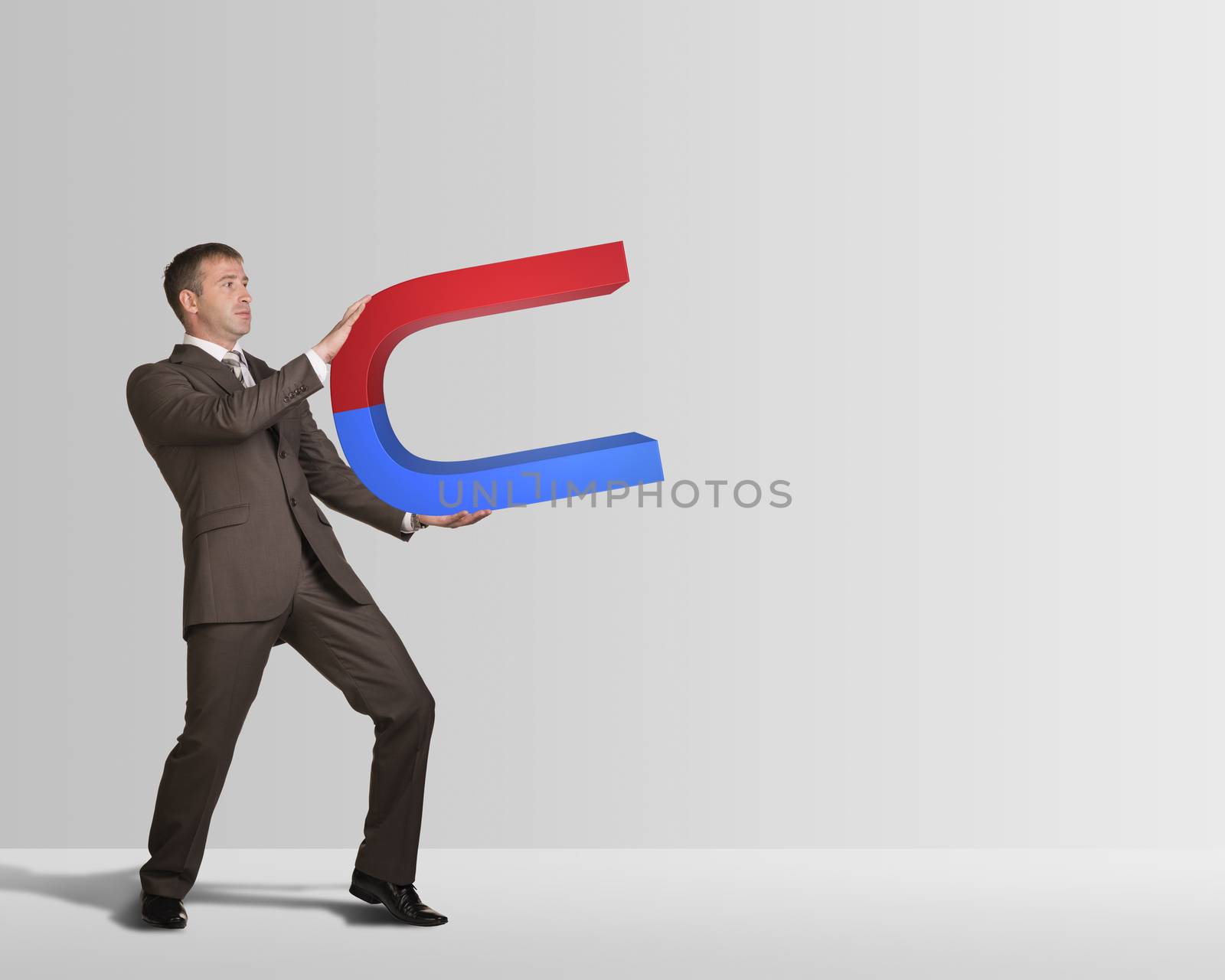 Businessman in suit holding big magnet by cherezoff