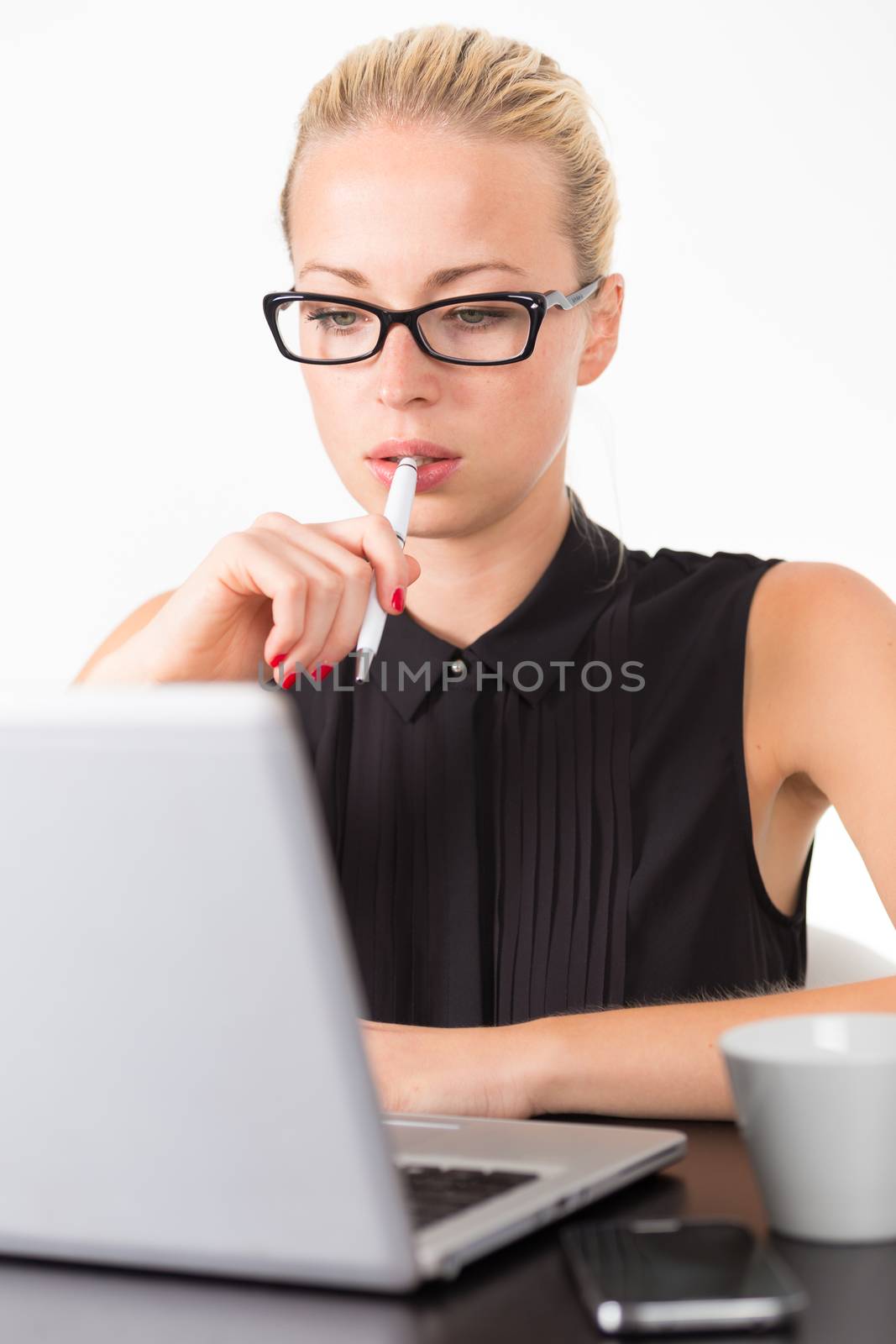 Business woman wearing black glasses, holding a pen in her hand, checking some information on her laptop computer in office. 