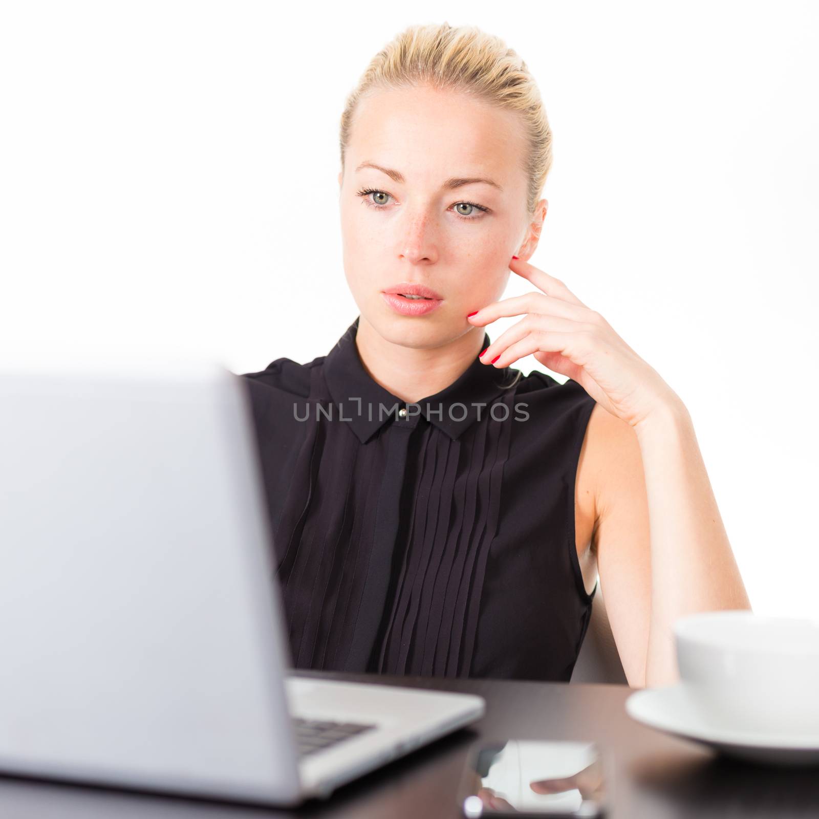 Business woman checking some information on her laptop computer in office. White cup of coffee on the desk. 