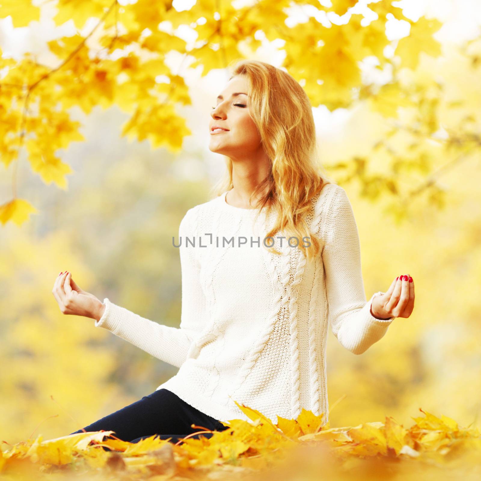 Beautiful young woman sitting in autumn park in lotus yoga position