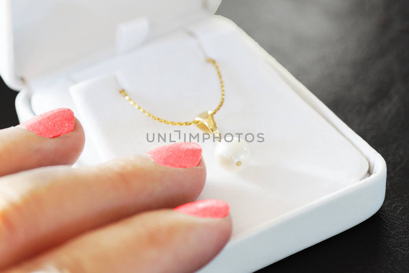 Woman fingers with pink nail polish on jewelry box with gold necklace with white pearl, gift and love concept