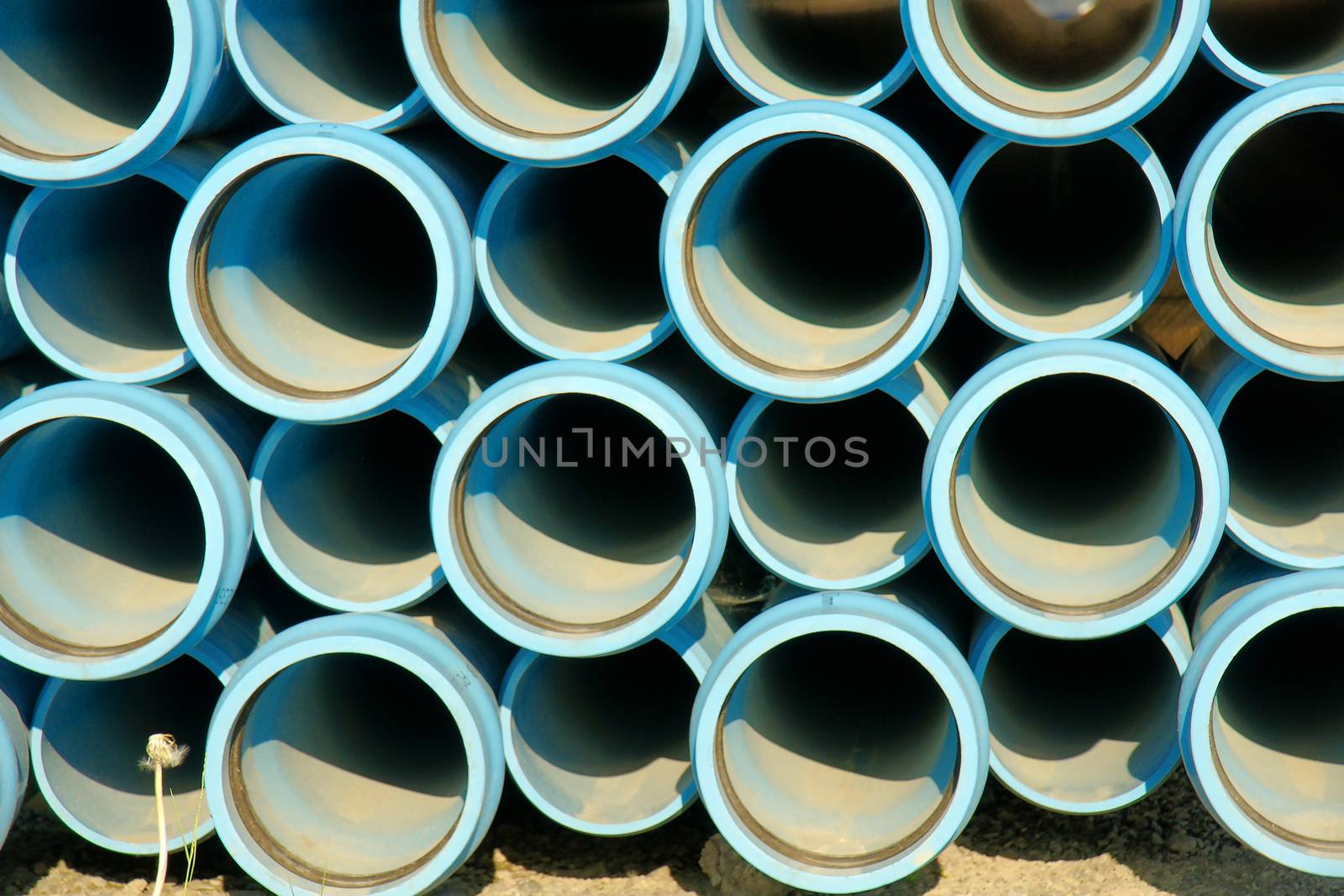 Front of stack of blue plastic PVC water pipe to be used in a new development of residental area, industrial background
