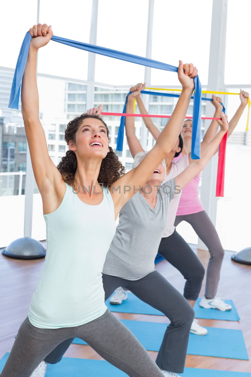 Happy female trainer with class holding up exercise belts at yoga class