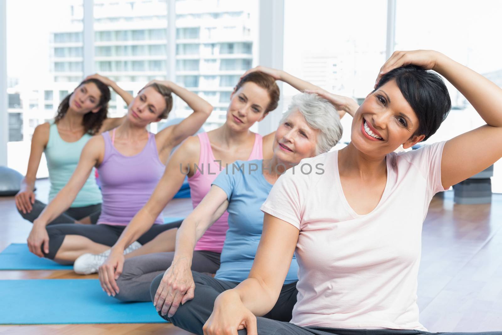 Female trainer with class stretching neck in row at yoga class