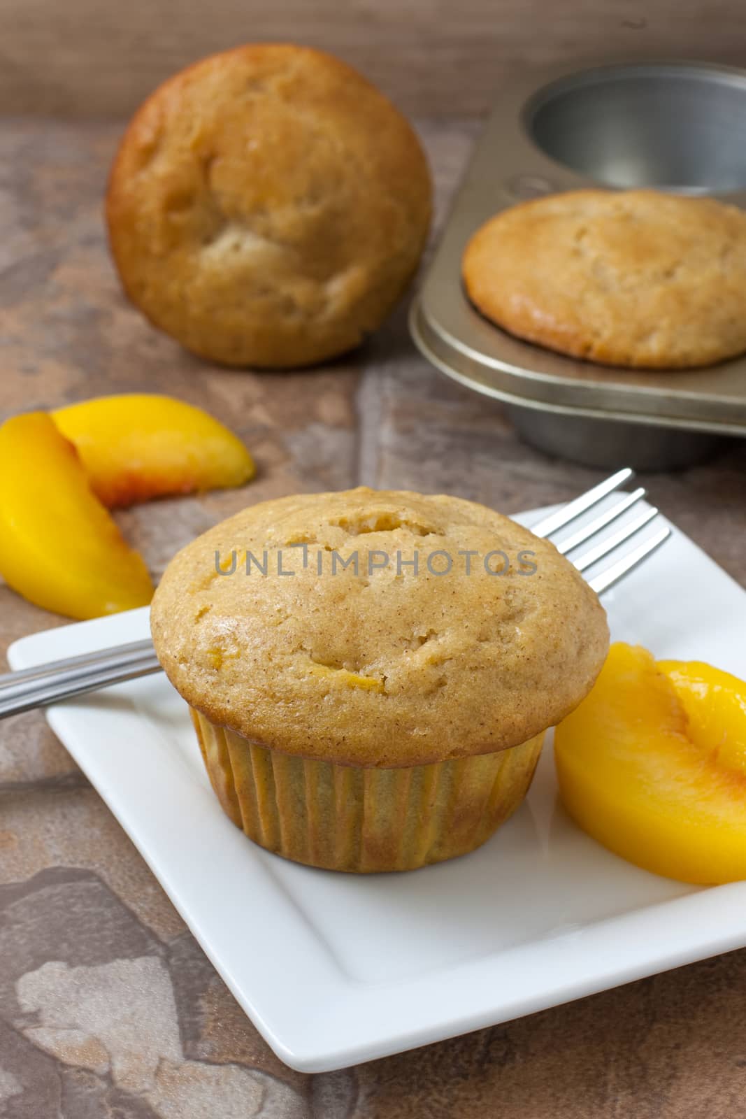 Homemade peach muffin with fresh peaches on a white plate sitting on a countertop.