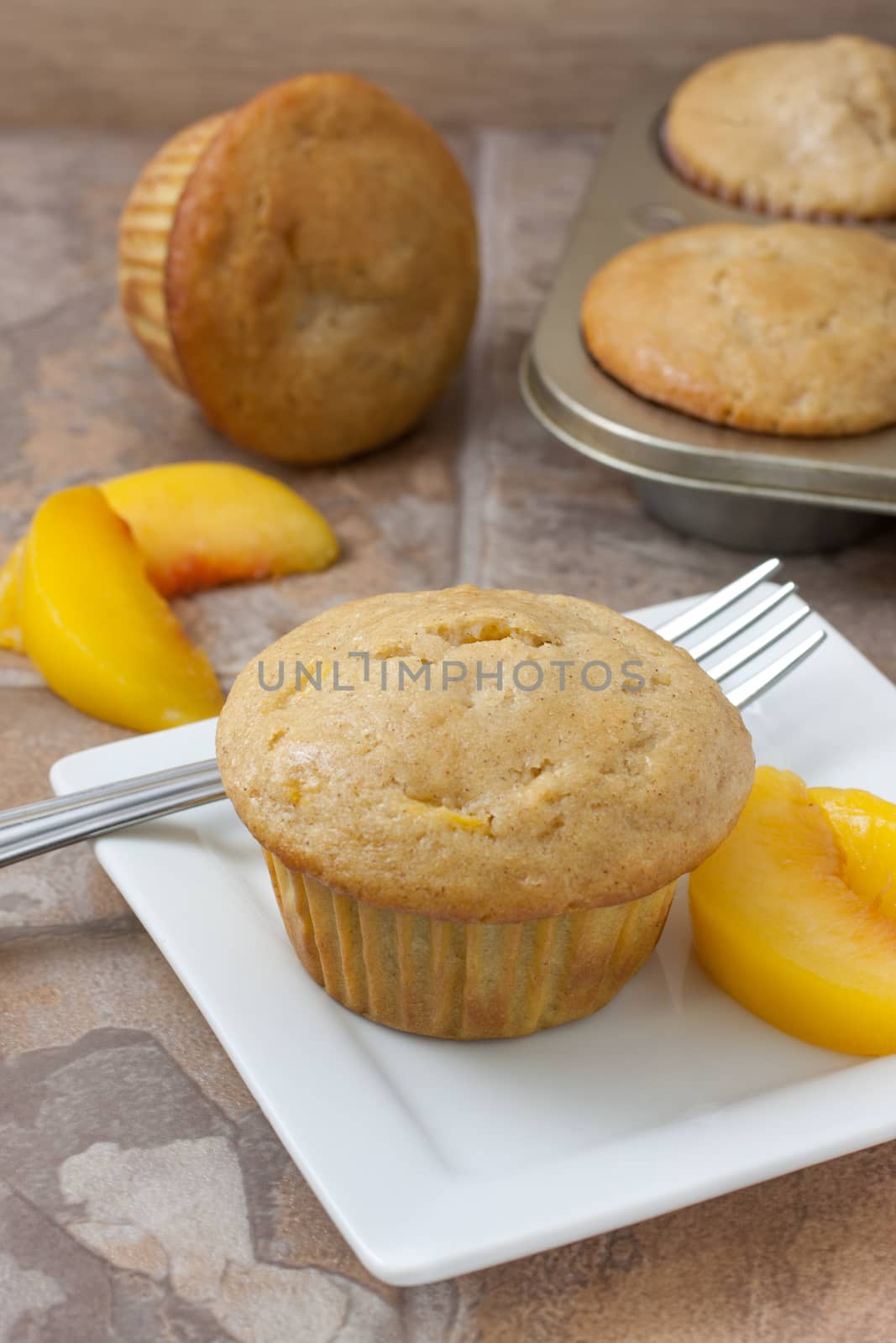 Homemade peach muffin with fresh peaches on a white plate sitting on a countertop.