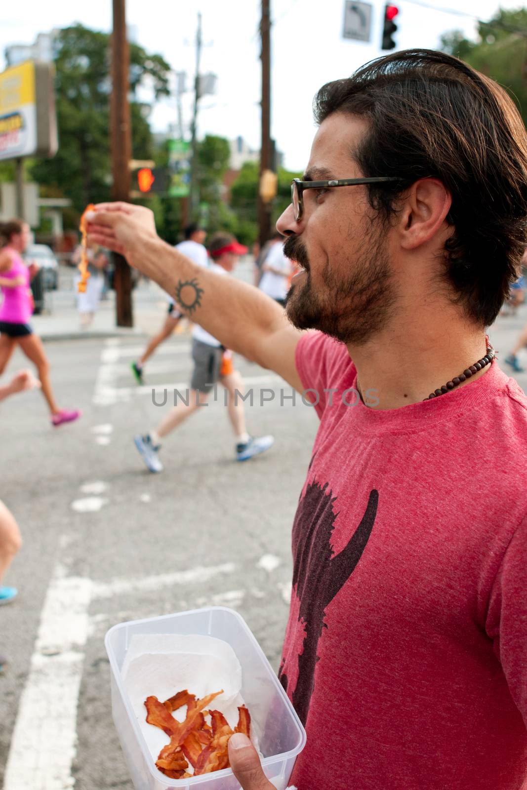 Atlanta, GA, USA - July 4, 2014:  An unidentified man gives out strips of bacon to exhausted runners as they near the finish line of the Peachtree Road Race.