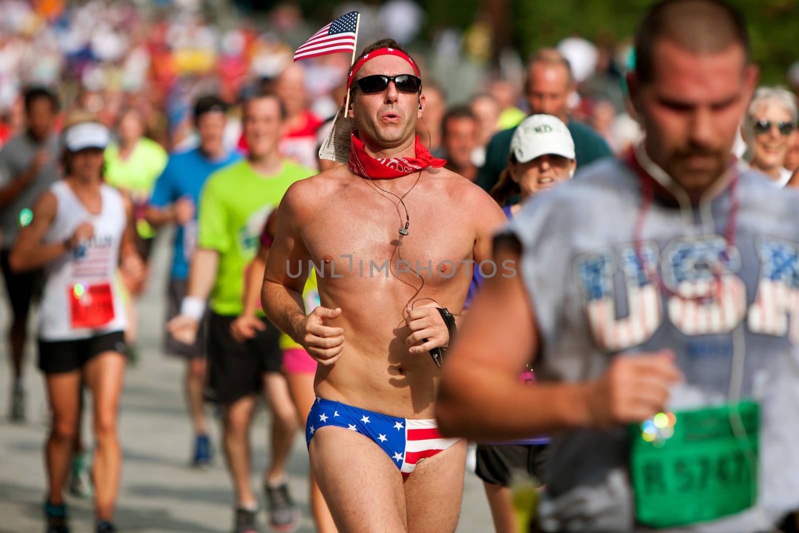 Atlanta, GA, USA - July 4, 2014:  A man running in a bikini swimsuit and with an American flag in his bandana, heads for the finish line of the Peachtree Road Race.