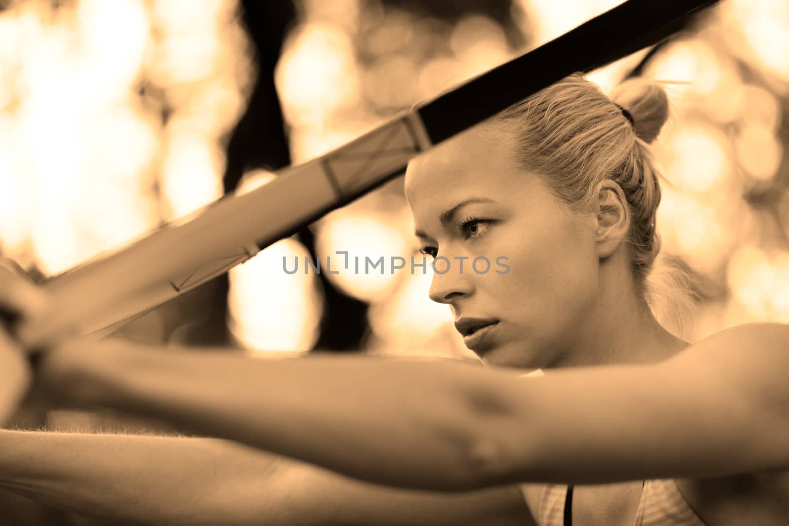 Young attractive woman does suspension training with fitness straps outdoors in the nature.