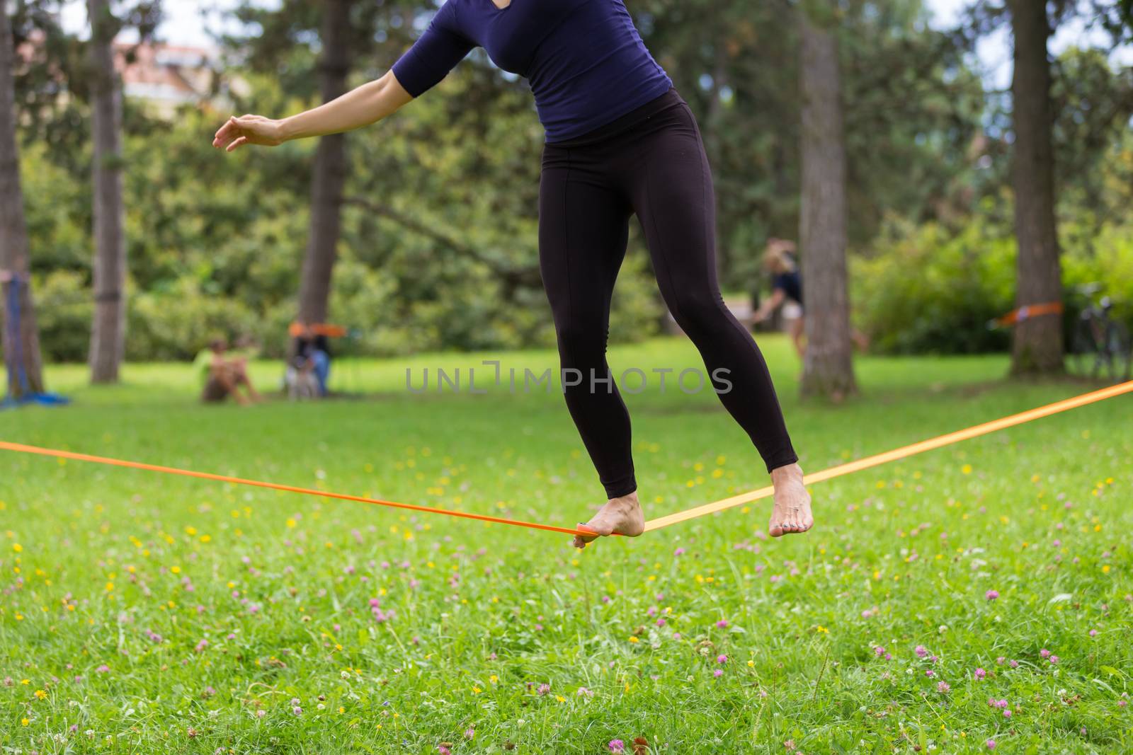 Lady practising slack line in the city park. Slacklining is a practice in balance that typically uses nylon or polyester webbing tensioned between two anchor points.