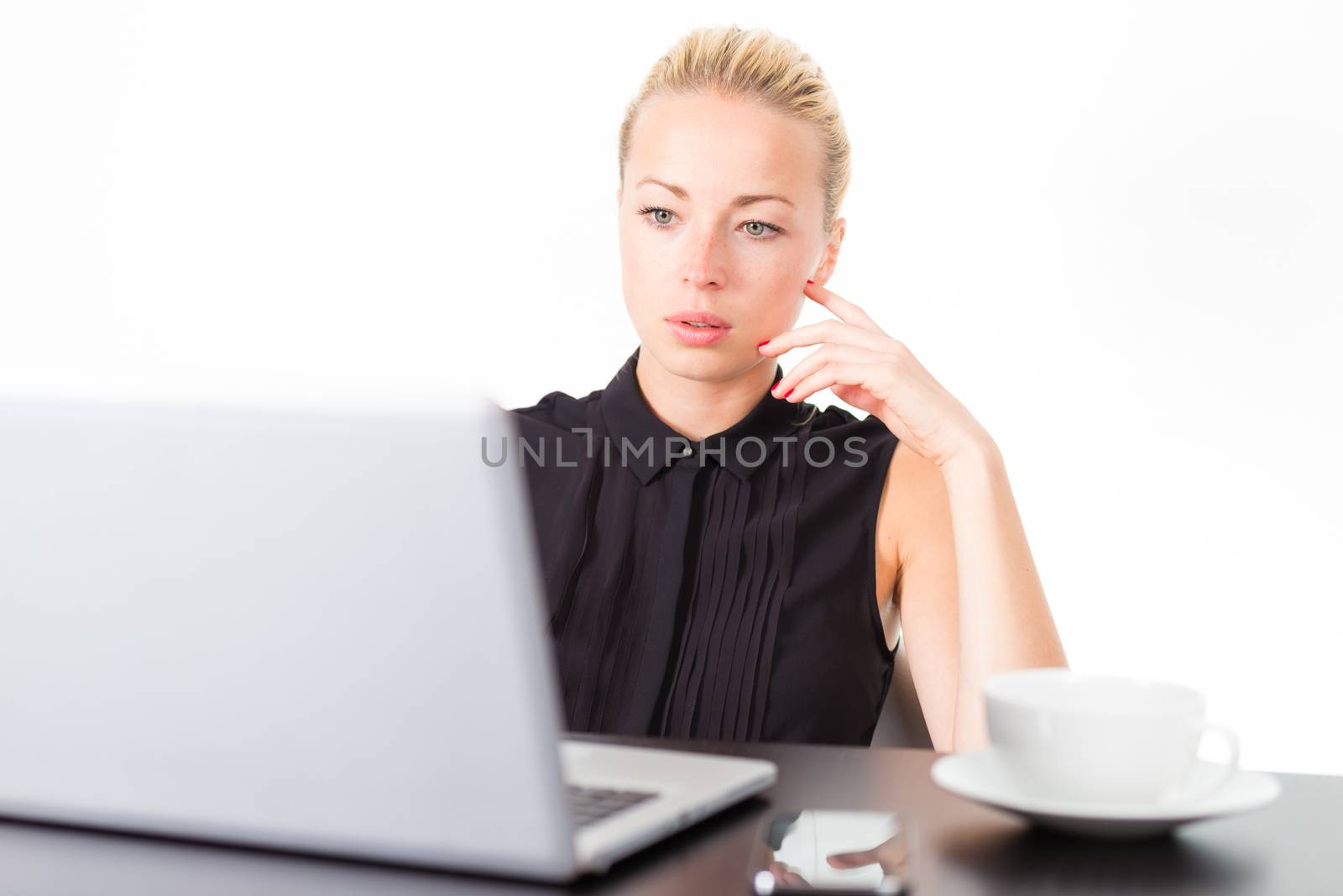 Business woman checking some information on her laptop computer in office. White cup of coffee on the desk. 