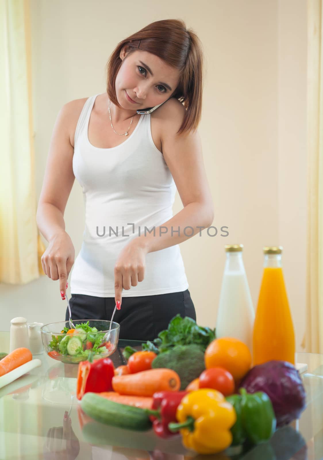 Young asian woman in kitchen and talking on the mobile phone by witthaya