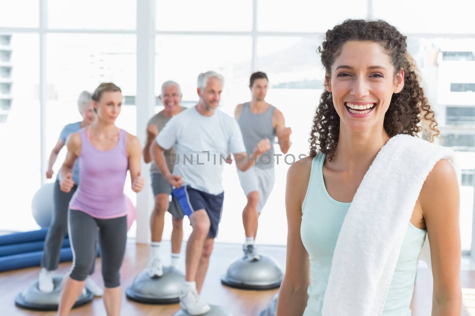 Portrait of a cheerful young woman with people exercising in the background at fitness studio