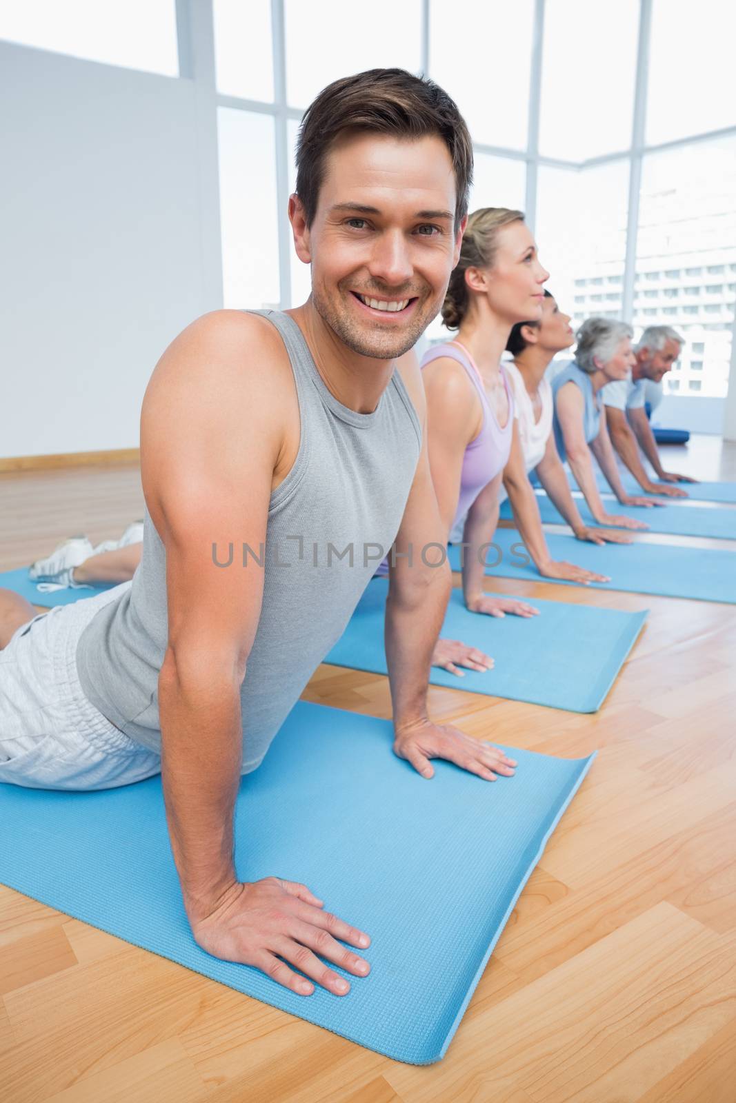 Fitness group doing cobra pose in row at the yoga class