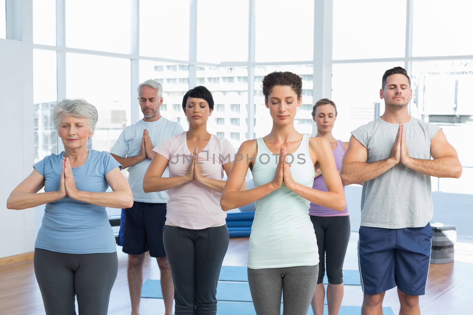 Sporty people with eyes closed and joined hands at a bright fitness studio