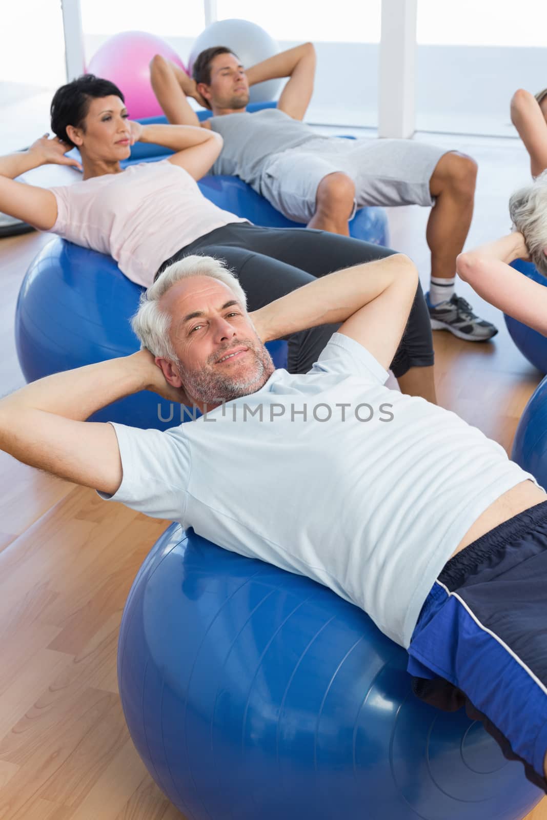 Portrait of smiling people stretching on exercise balls in the bright gym