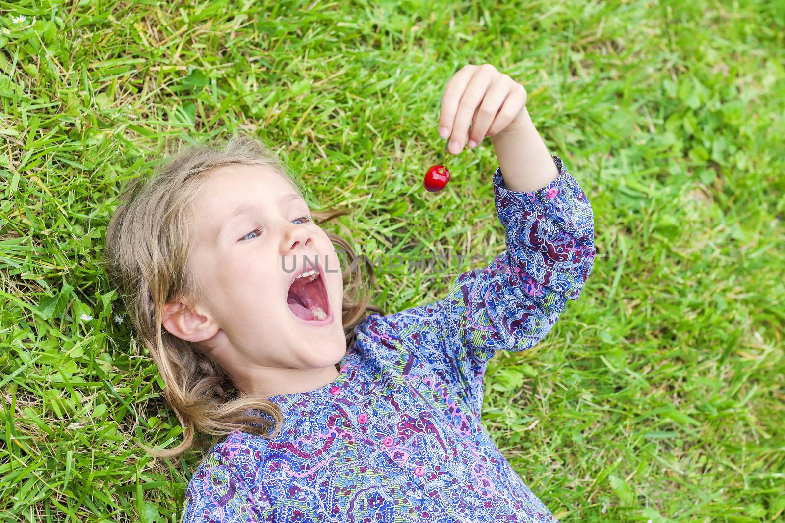 little girl lying on the grass with cherry in the hand 
