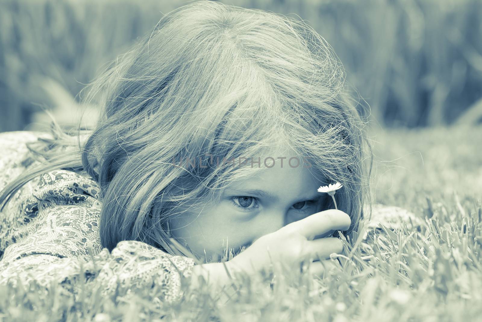 Little adorable blond girl lying on grass looking at daisy 