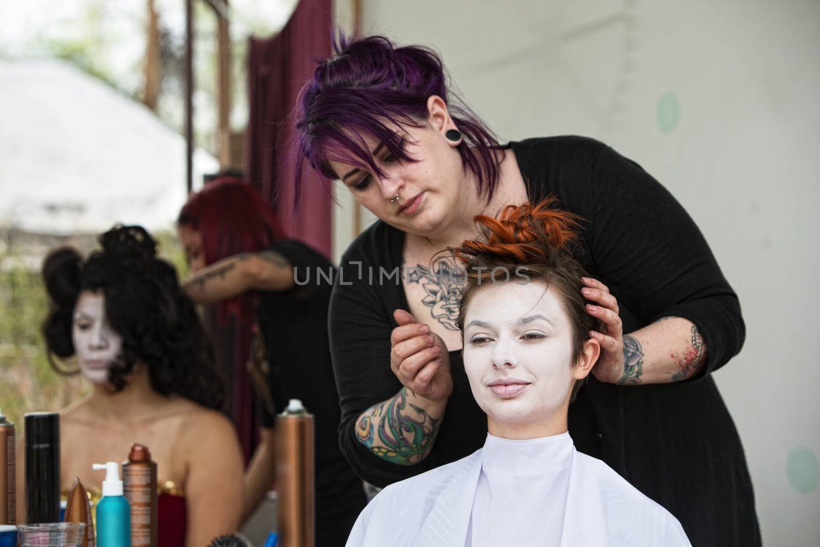 Stylist with tattoo fixing hair for woman in white makeup