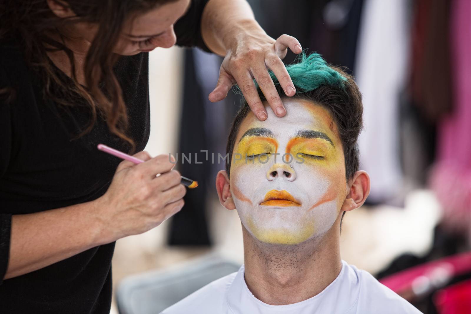 Young male clown getting makeup on face