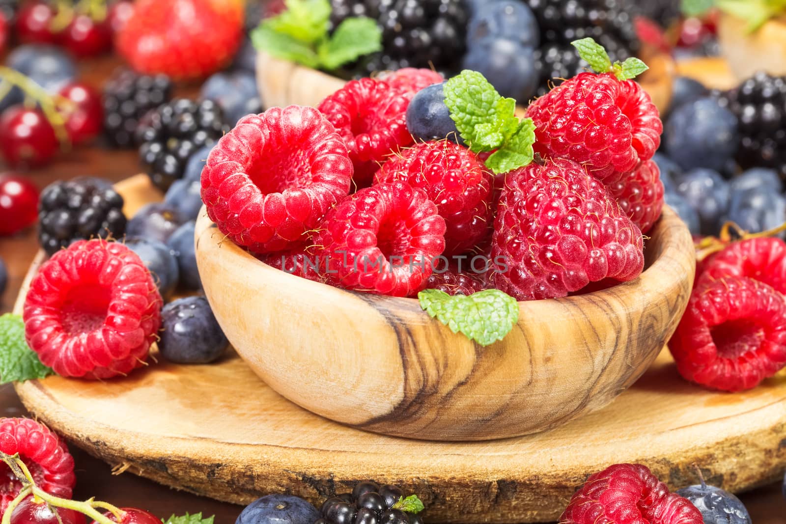 Fresh raspberries in an olive wood bowl and different fresh berries. Focus on raspberries. Macro, selective focus