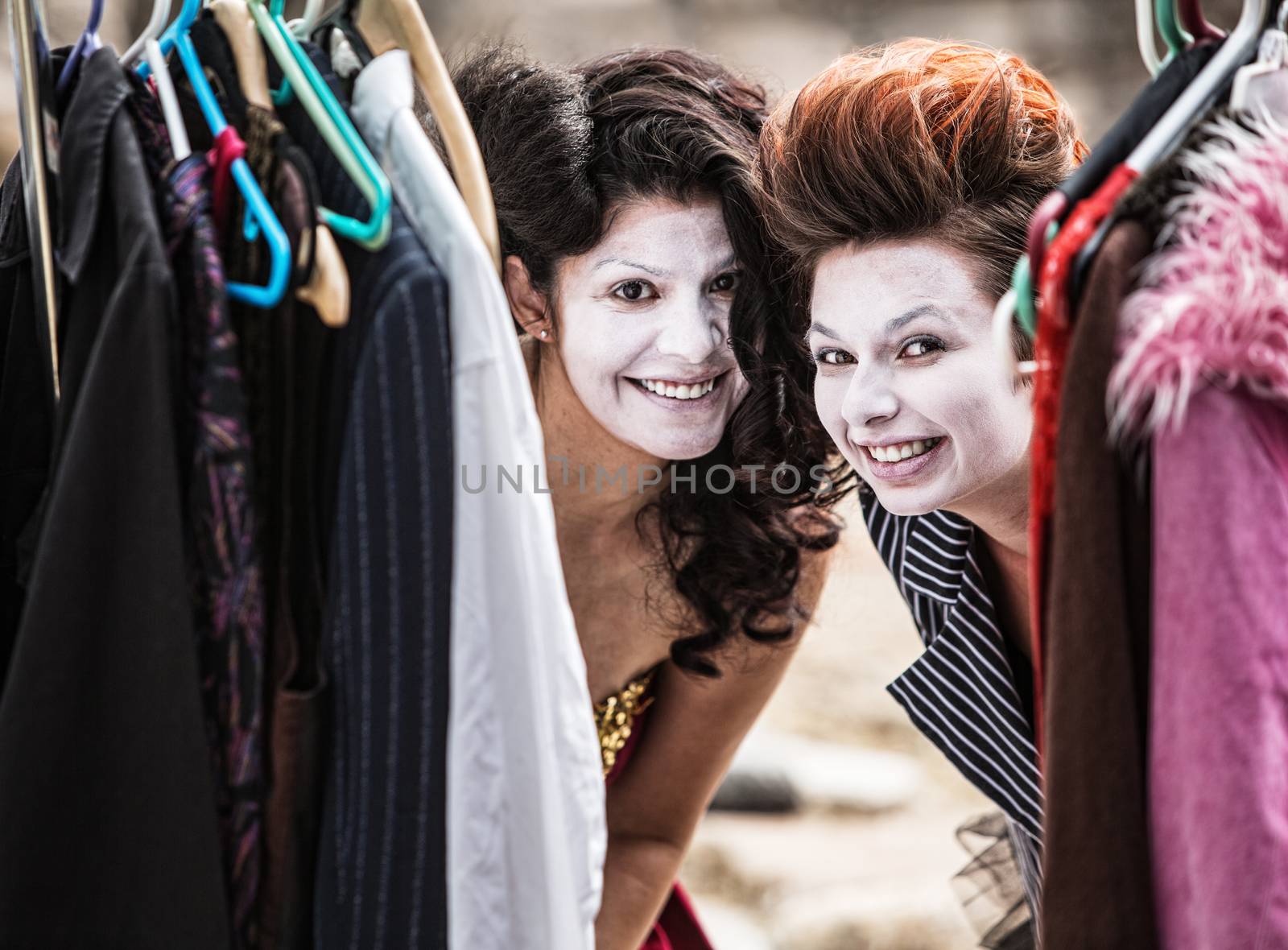 Pair of young cirque clowns peeking from clothing rack